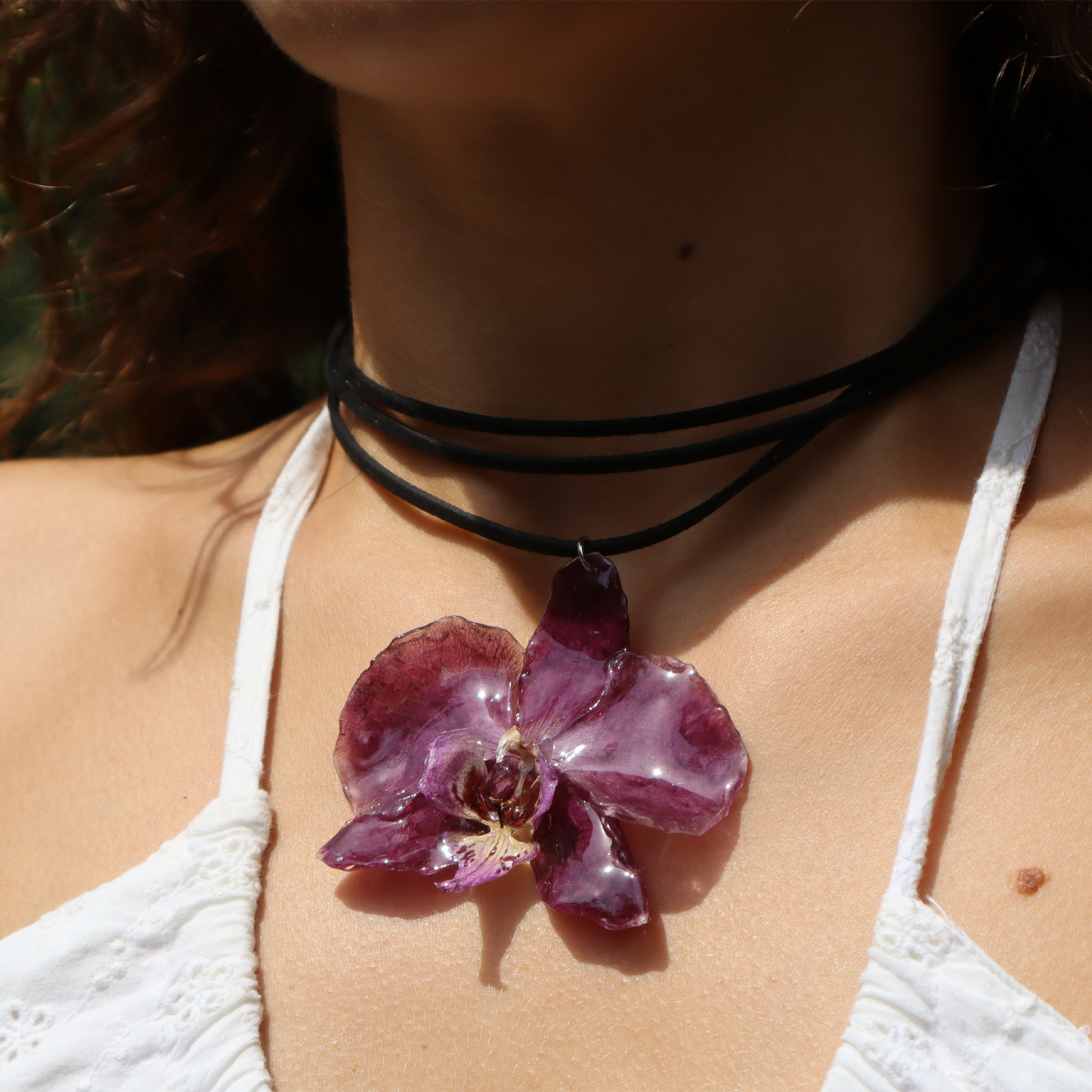 Mujer llevando choker violeta artesanal con flor de orquídea natural y cordón de cuero
